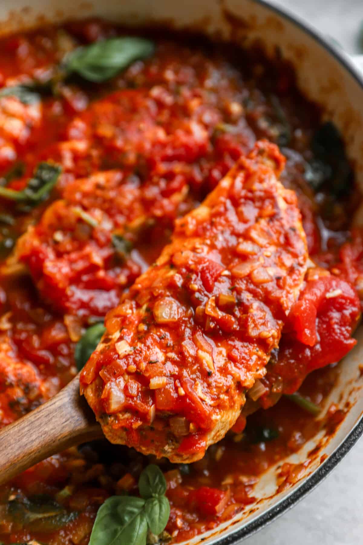 Italian chicken in tomato sauce being lifted out of a pan.