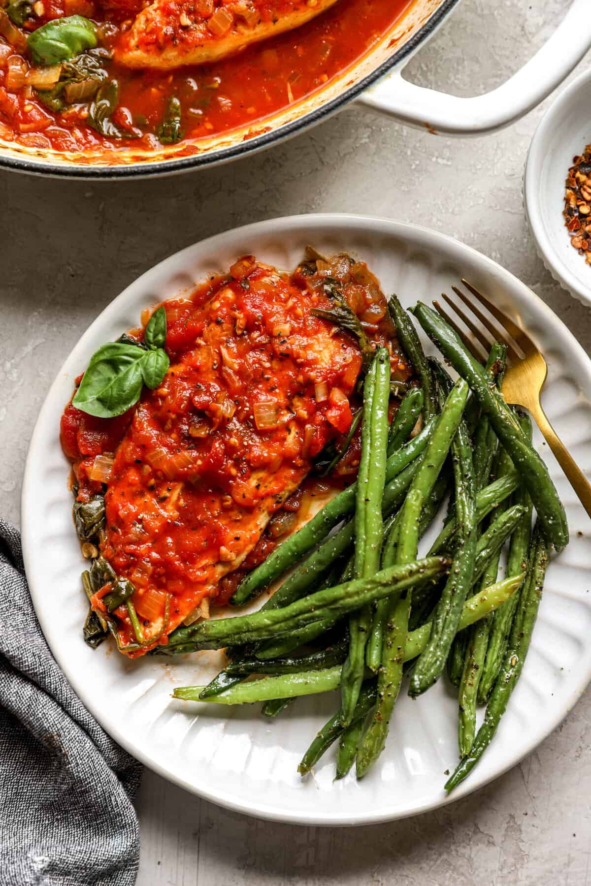 above image of a chicken cutlet with tomato sauce and green beans on a plate.