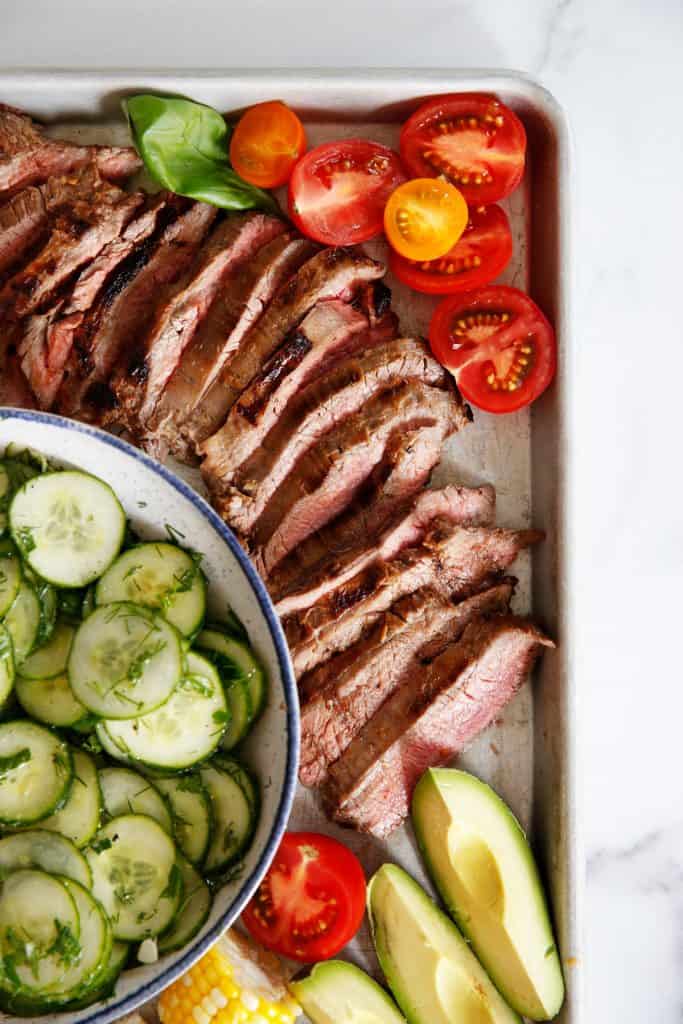 A platter of flank steak surrounded by salads and tomatoes.