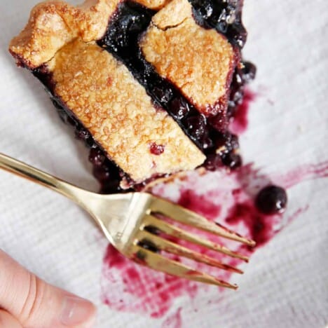 A slice of gluten-free blueberry pie on a plate with a bite taken out of it.