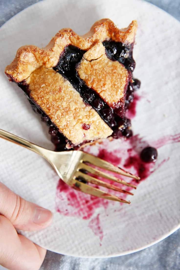 A slice of gluten-free blueberry pie on a plate with a bite taken out of it.