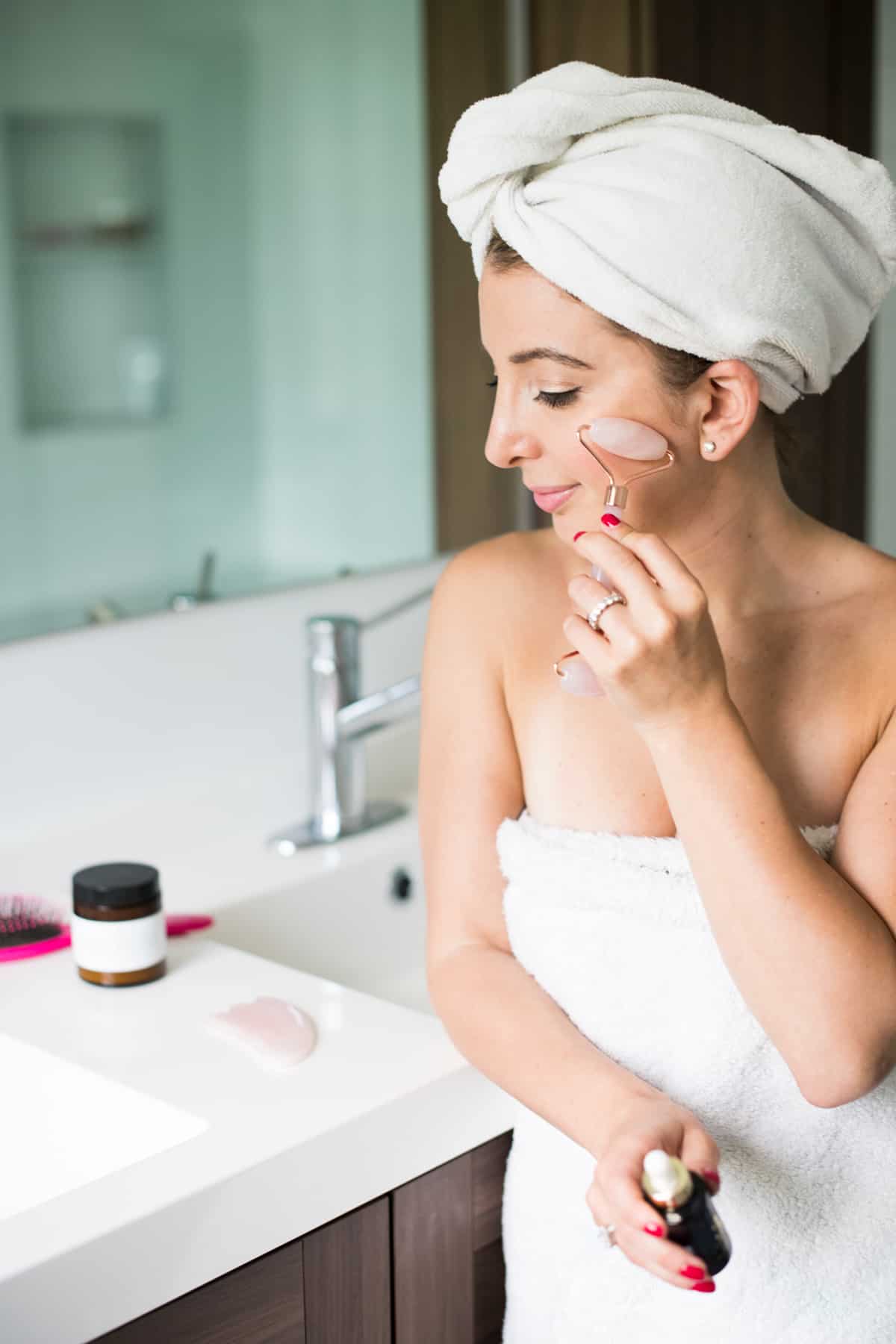 A woman in a towel using a jade roller on her skin.