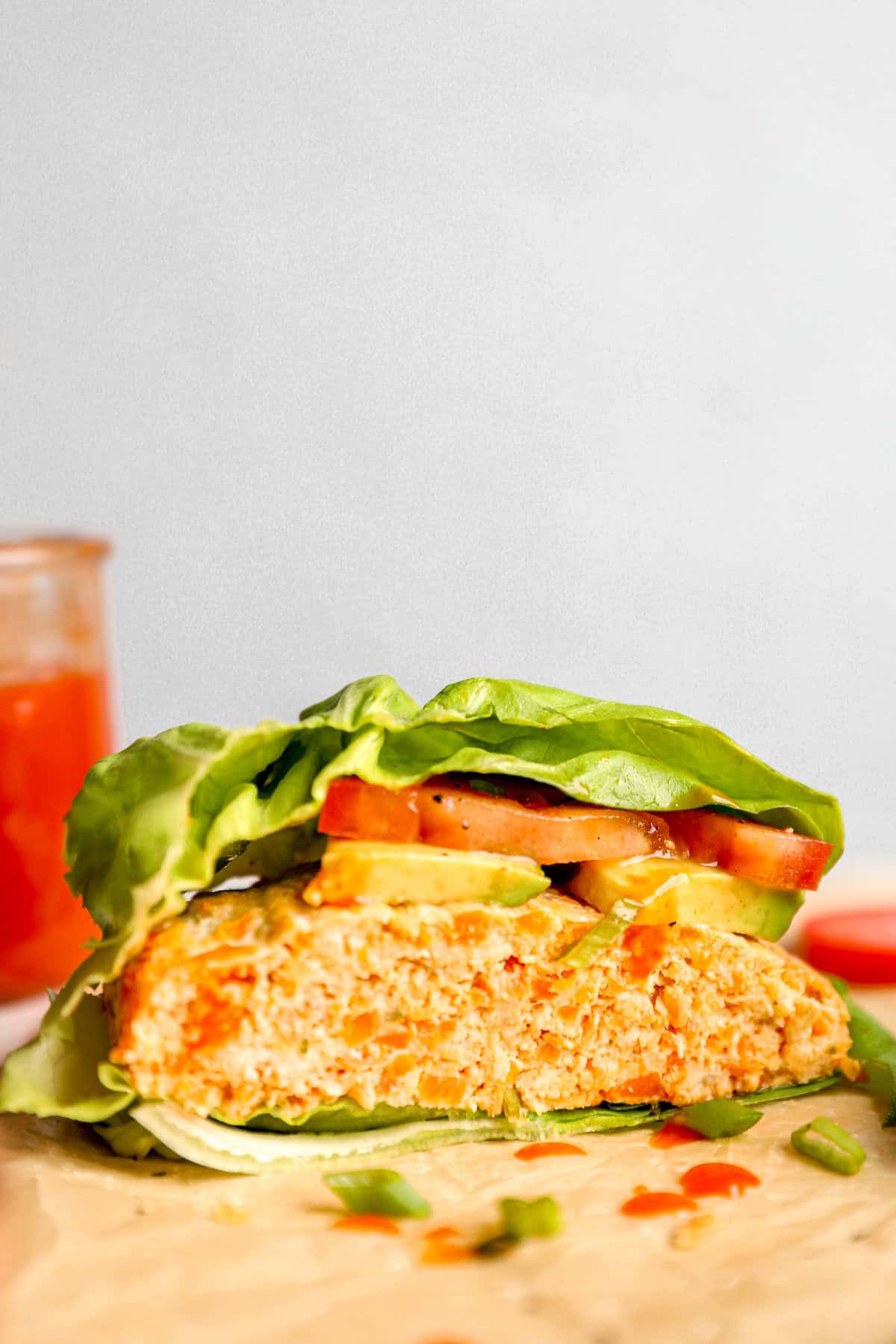 side view of a lettuce wrapped chicken burger topped with tomato.