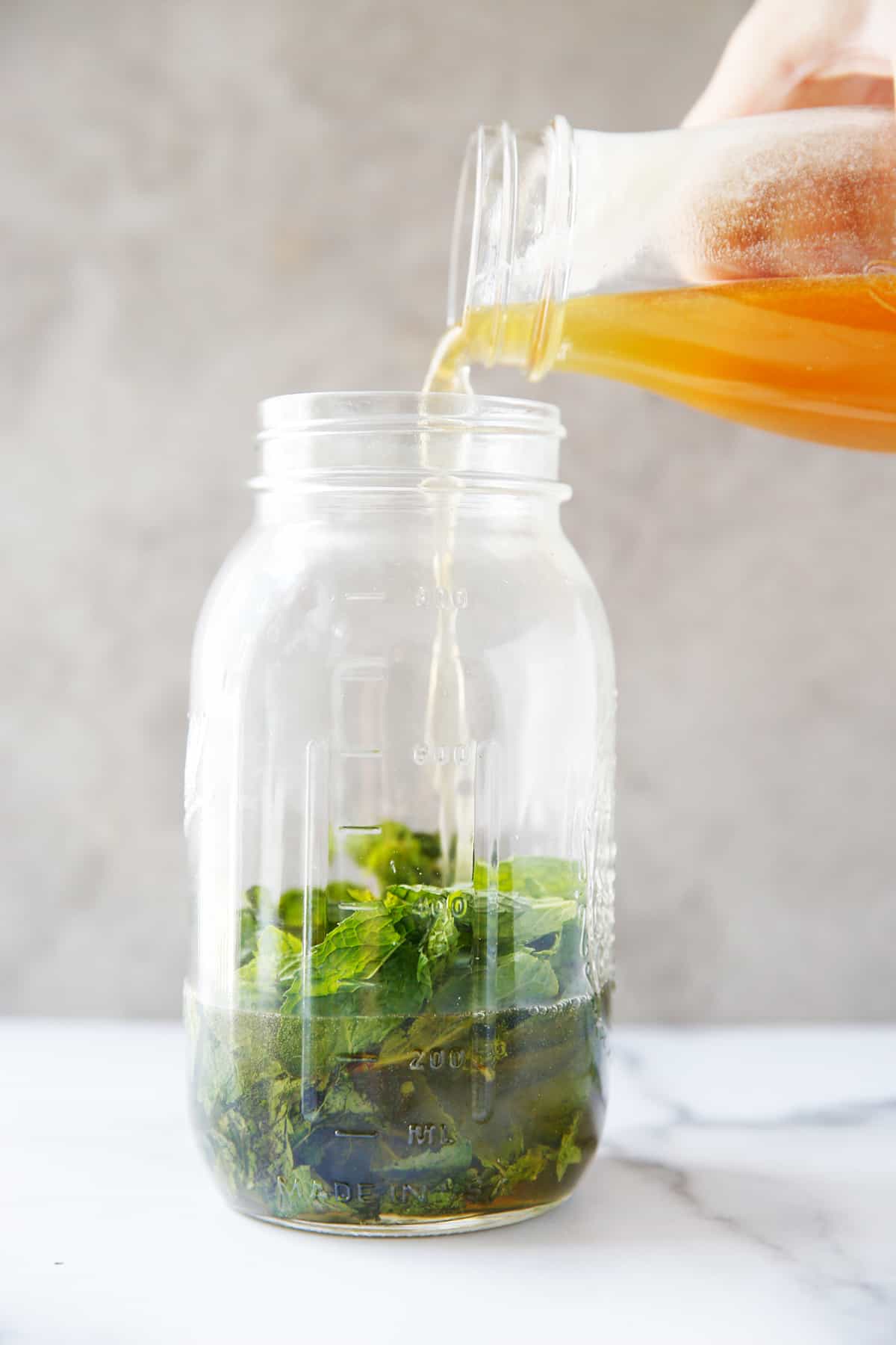 Pouring simple syrup made with honey over fresh mint leaves