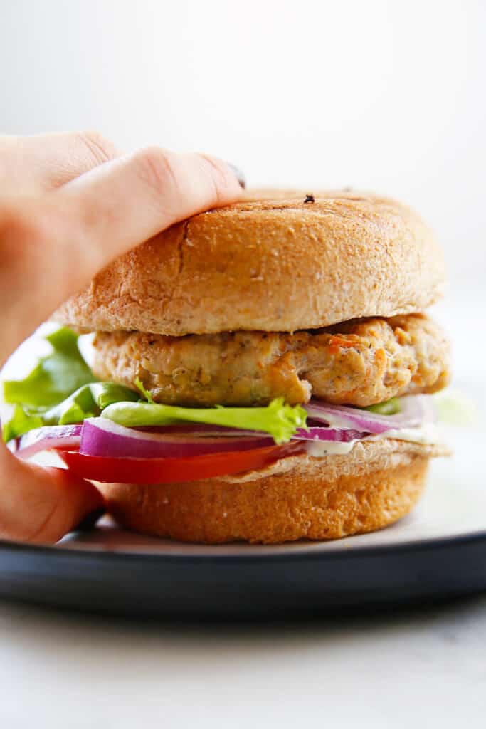 A chicken burger on a plate with lettuce and other toppings.