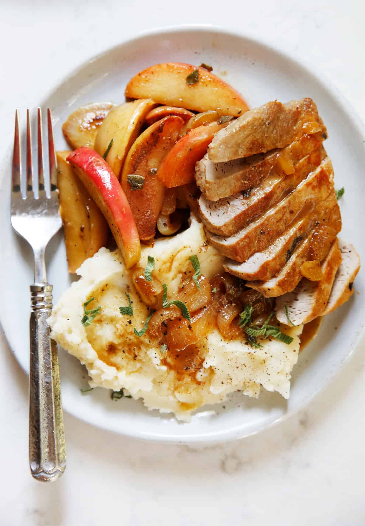 A plate of apple pork chops with onions and mashed potato.