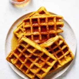 A plate of gluten free pumpkin waffles with a jar of syrup on the side.