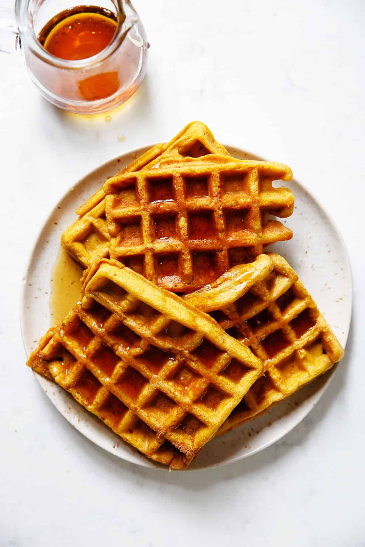 A plate of gluten free pumpkin waffles with a jar of syrup on the side.