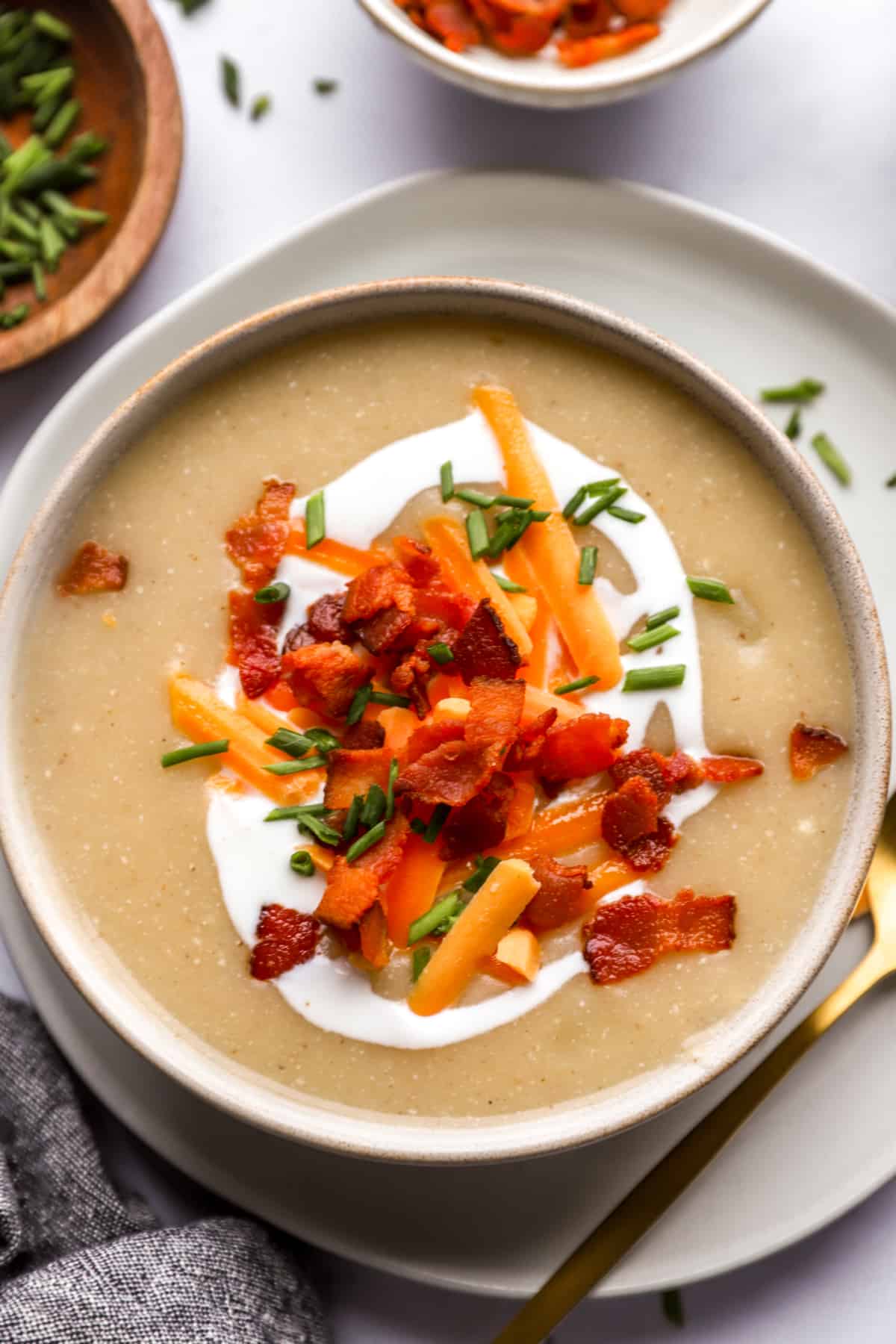 above image of a bowl of loaded potato soup topped with bacon, cheese, sour cream, and chives.