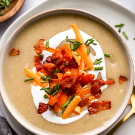 above image of a bowl of loaded potato soup topped with bacon, cheese, sour cream, and chives.