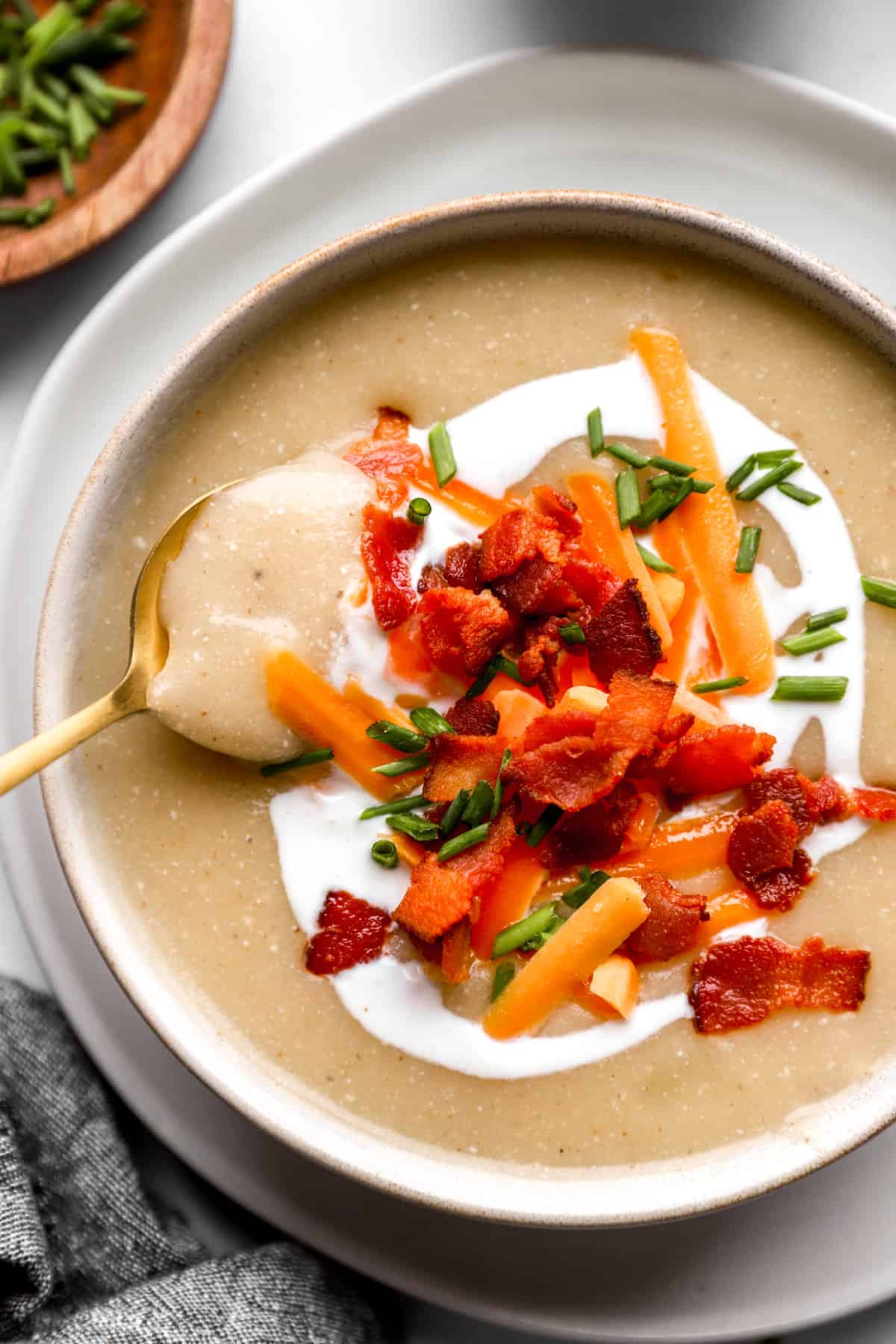 Pictured above is a bowl of soup filled with potatoes and topped with bacon, cheese, sour cream and chives.