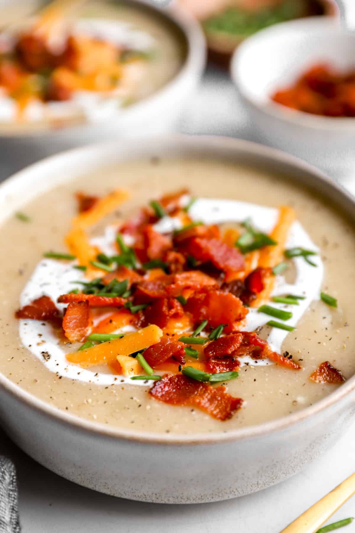 side view of a bowl of potato soup with baked potato toppings.