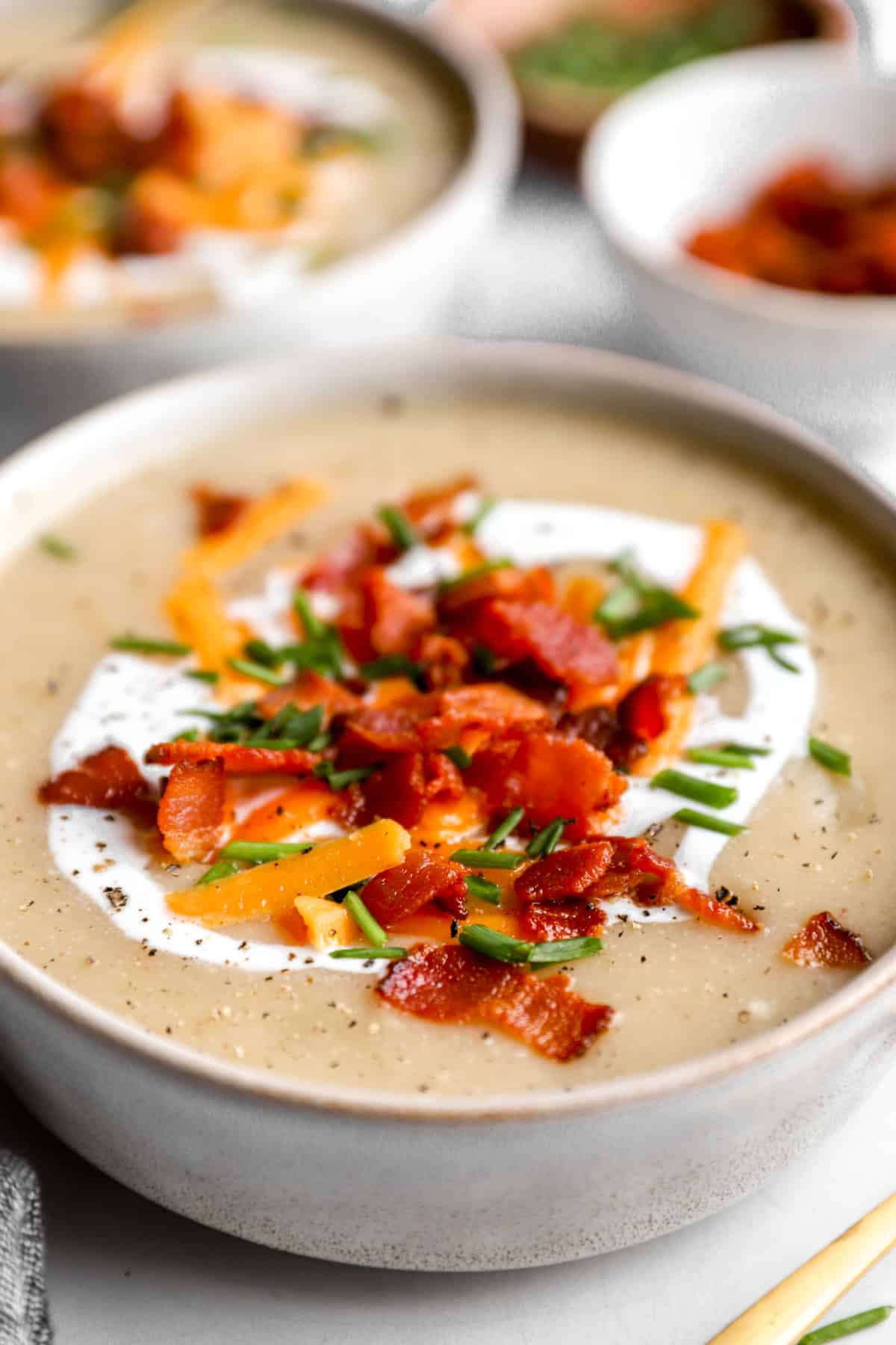 Side view of a bowl of potato soup with baked potato ingredients.