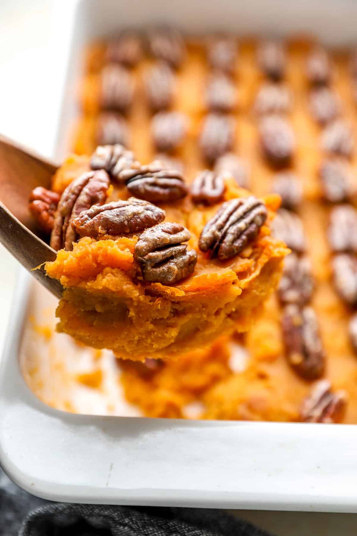 Sweet potato casserole with candied pecans on a wooden spoon being prepared to serve.