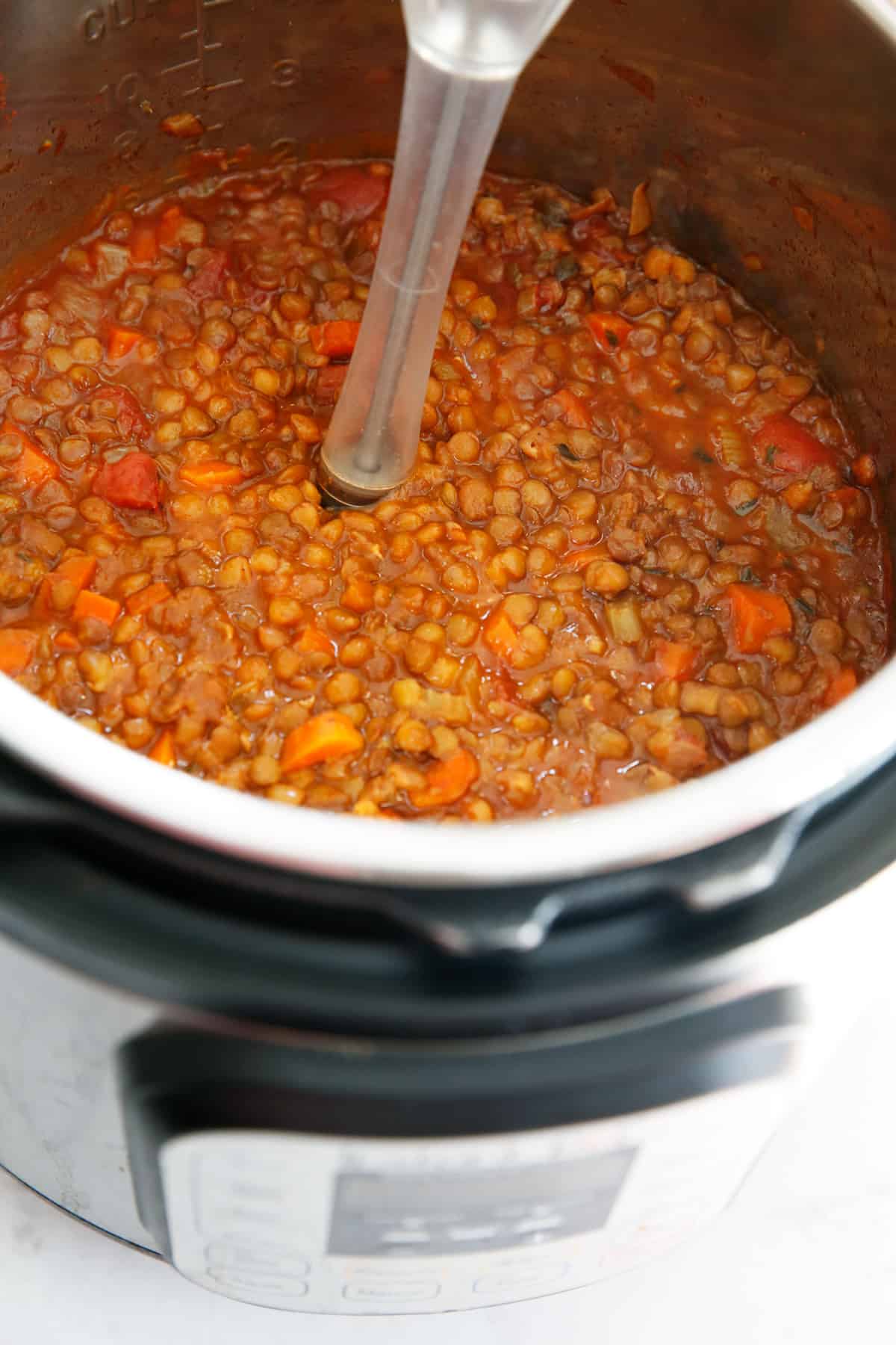 Instant pot lentil soup being partially pureed with a hand blender
