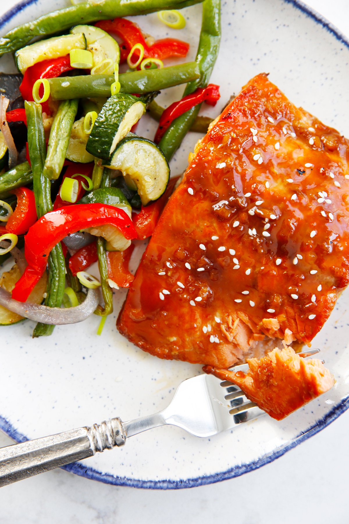 A fork full of asian glazed salmon on a plate.