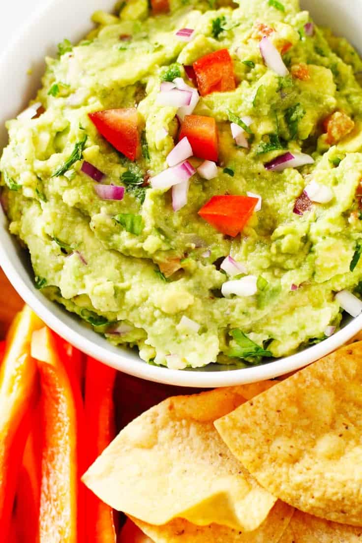 Guacamole with cut vegetables and tortilla chips.