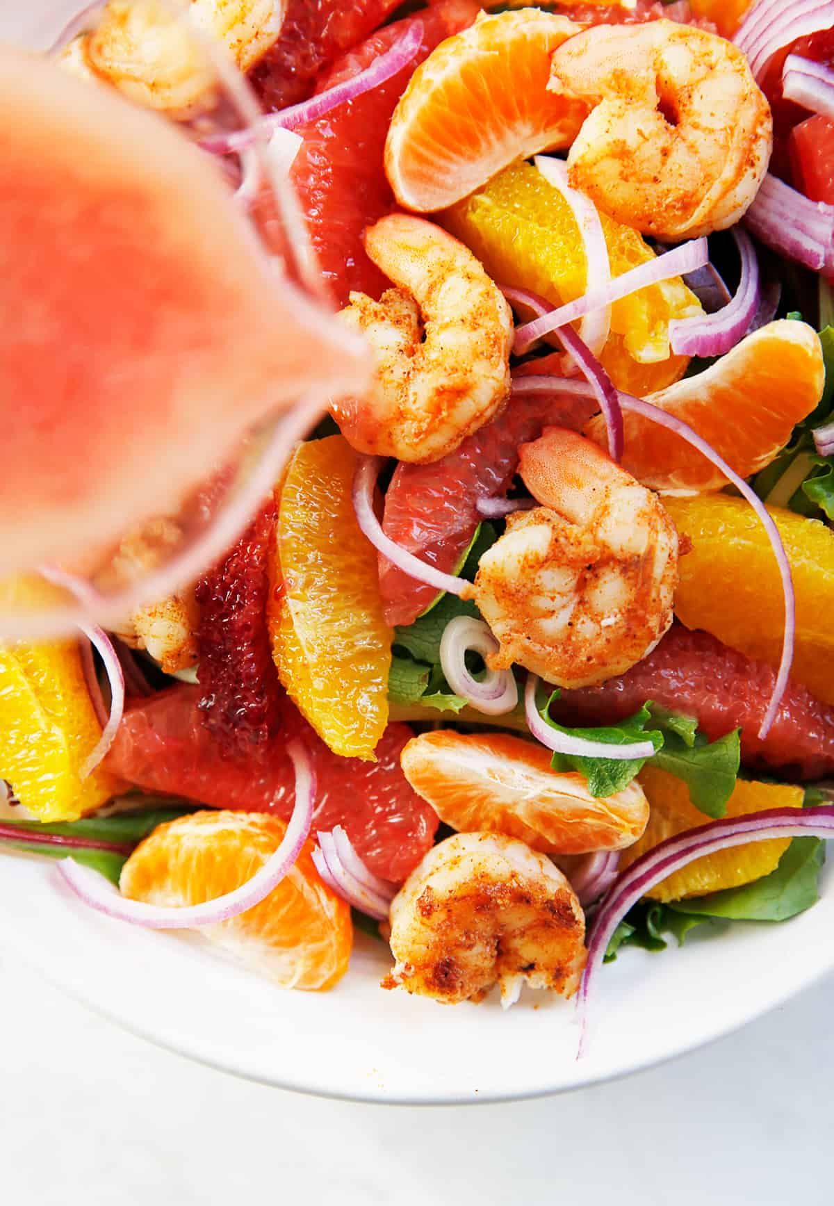 Grapefruit vinaigrette being poured over citrus shrimp salad.