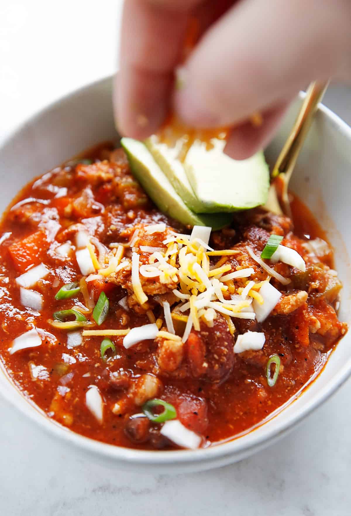 A hand sprinkling cheese on turkey chili in a bowl.