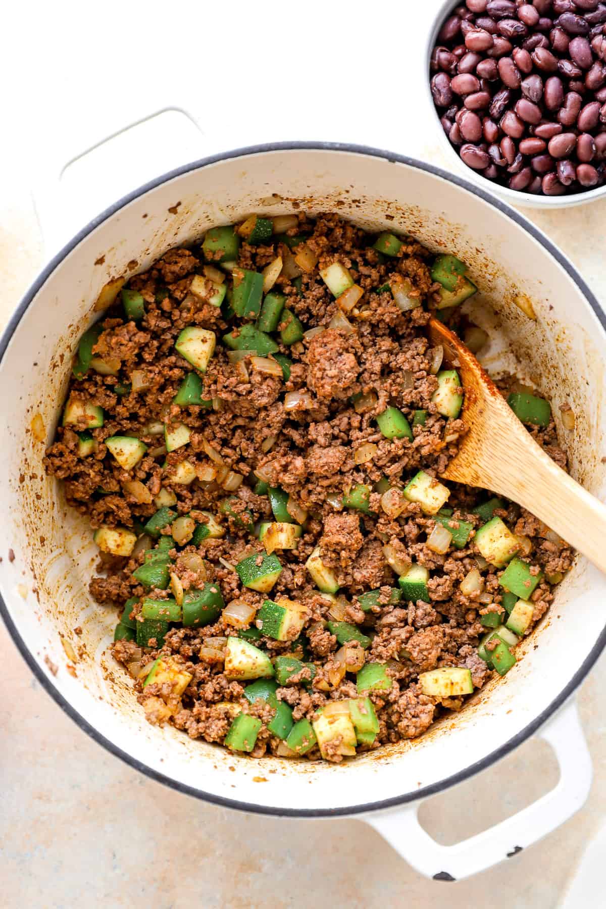 Dutch oven with a wooden spoon, filled with browned beef and sautéed vegetables.