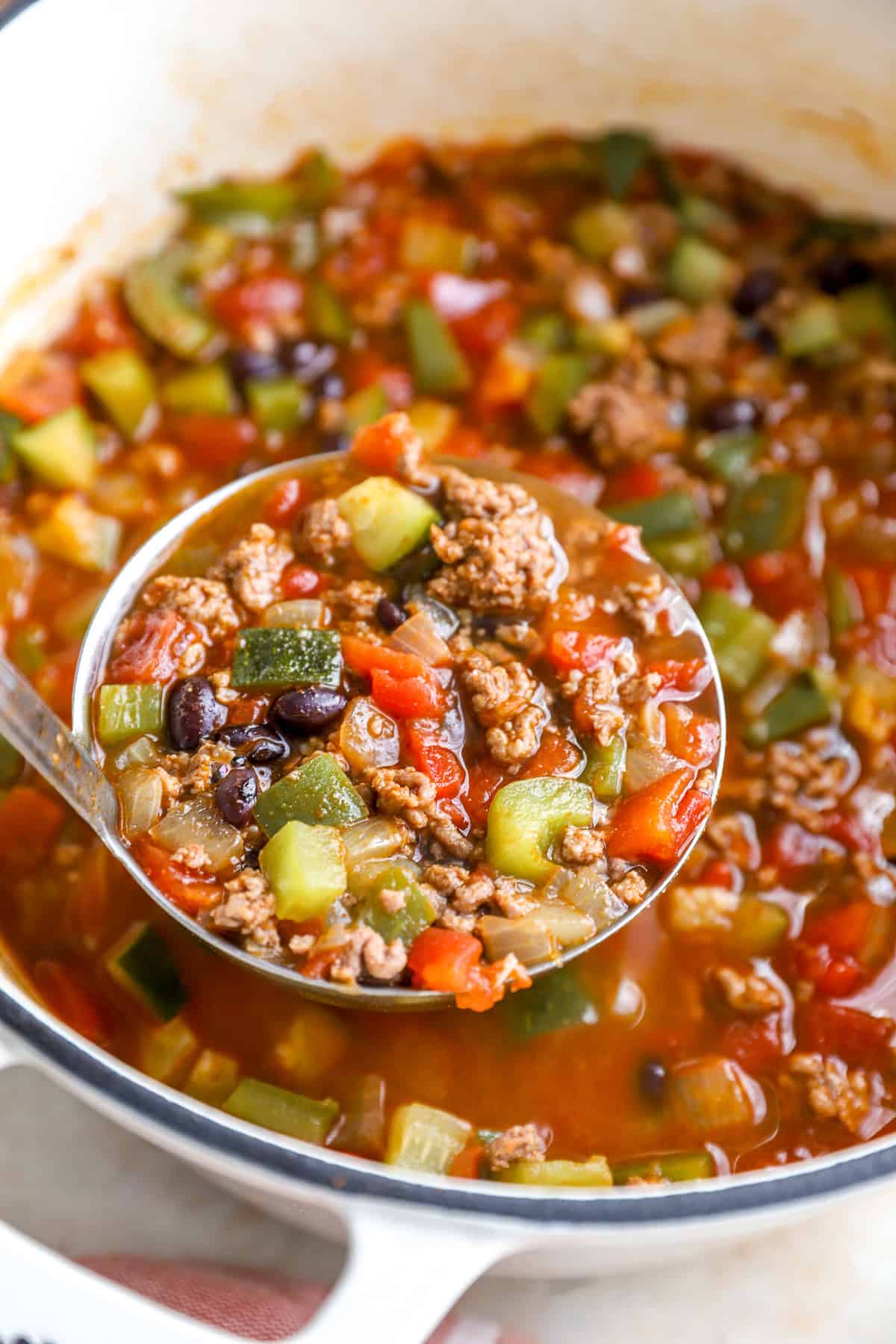 Ladle lifting taco soup with ground beef, zucchini, and tomatoes from the pot.