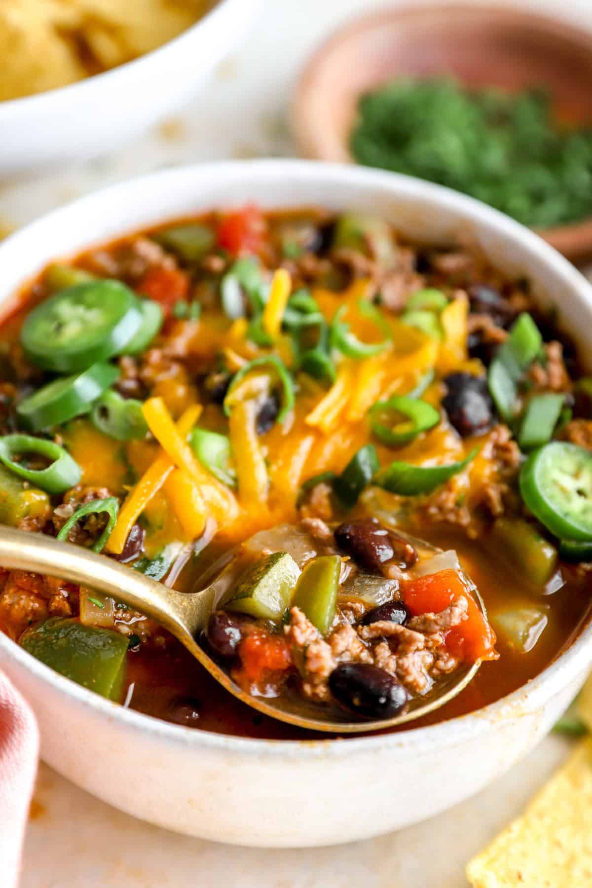 Bowl of taco soup topped with cheese, scallions and fresh jalapenos.
