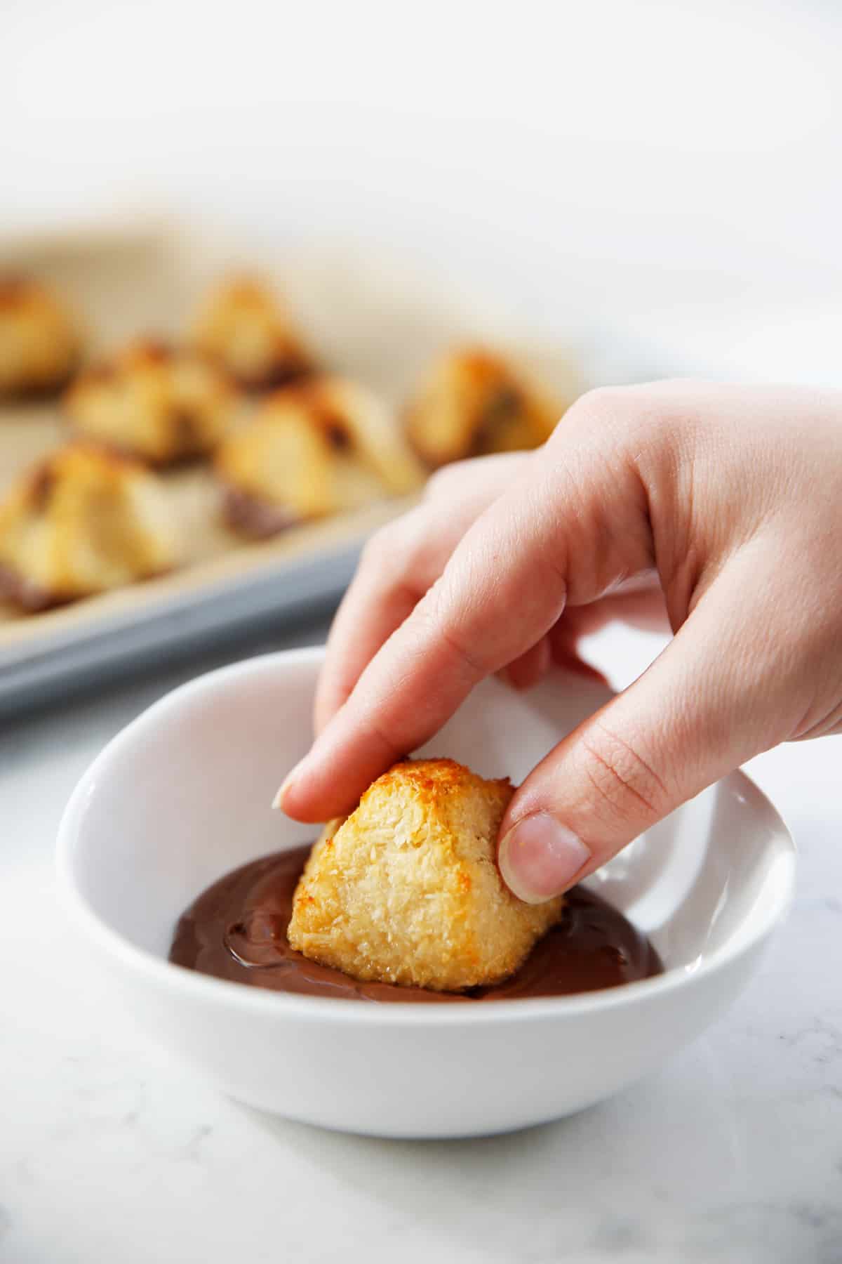 Dipping coconut macaroon in melted chocolate.