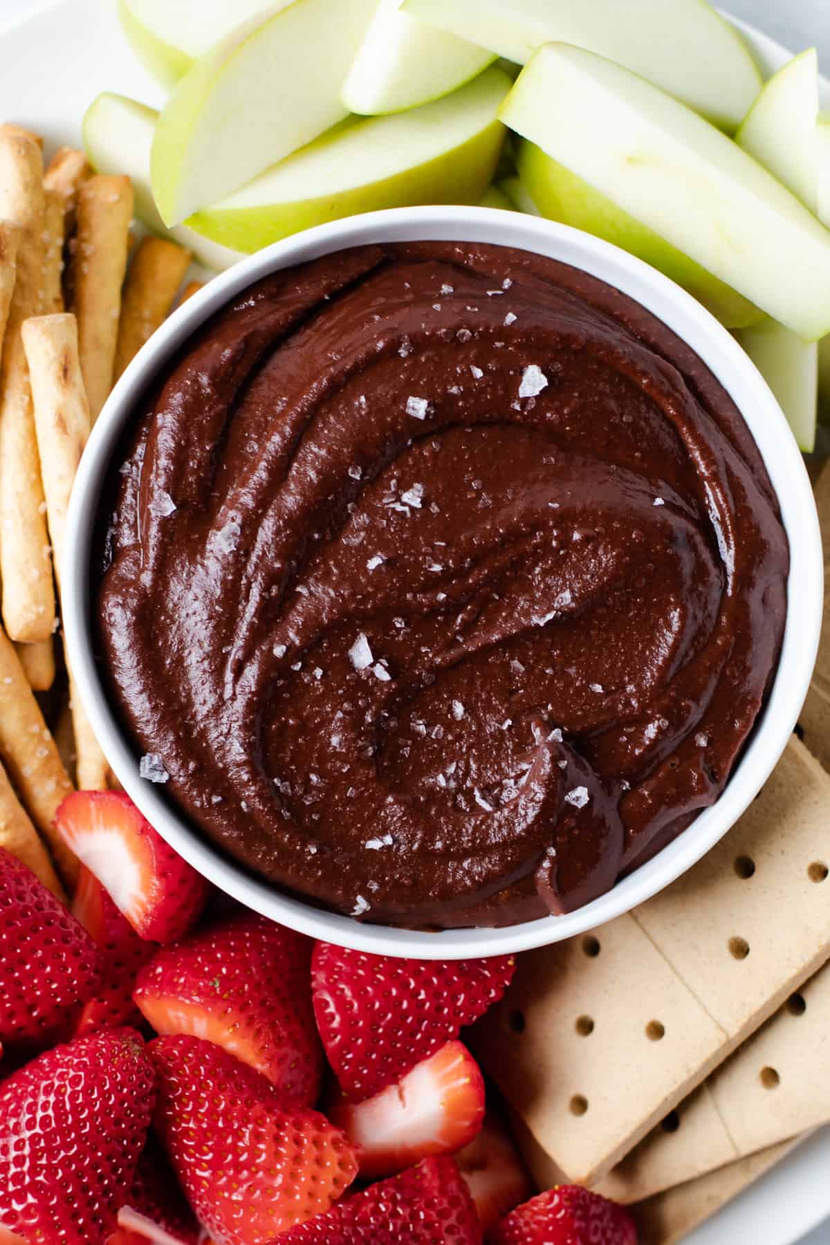A bowl of chocolate hummus with food to dip it in.