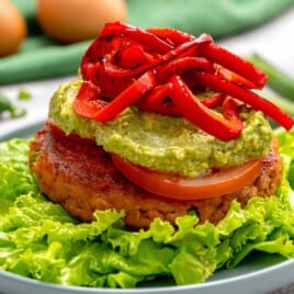 A salmon burger topped with guacamole and roasted red peppers.