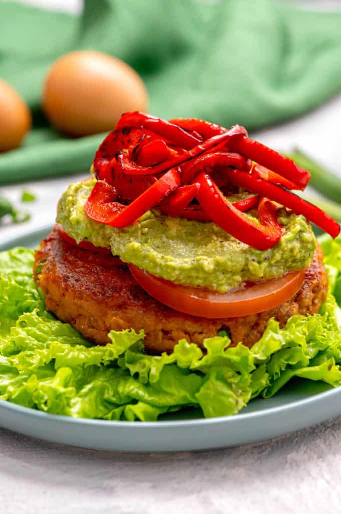 A salmon burger topped with guacamole and roasted red peppers.