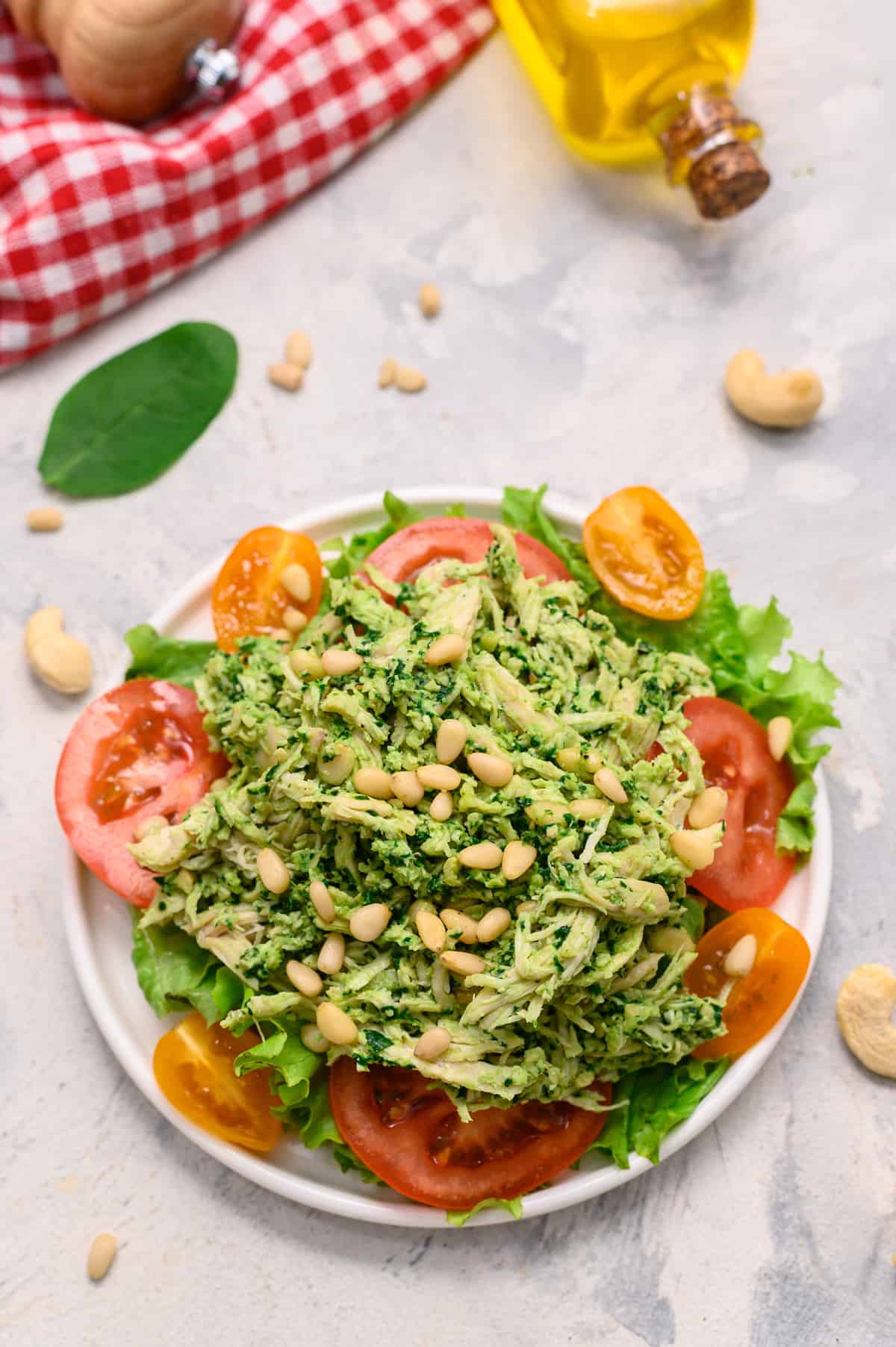 Chicken salad with pesto on a plate served over a bed of lettuce and tomatoes.