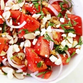 A bowl of watermelon salad with onions, herbs, cheese and nuts.