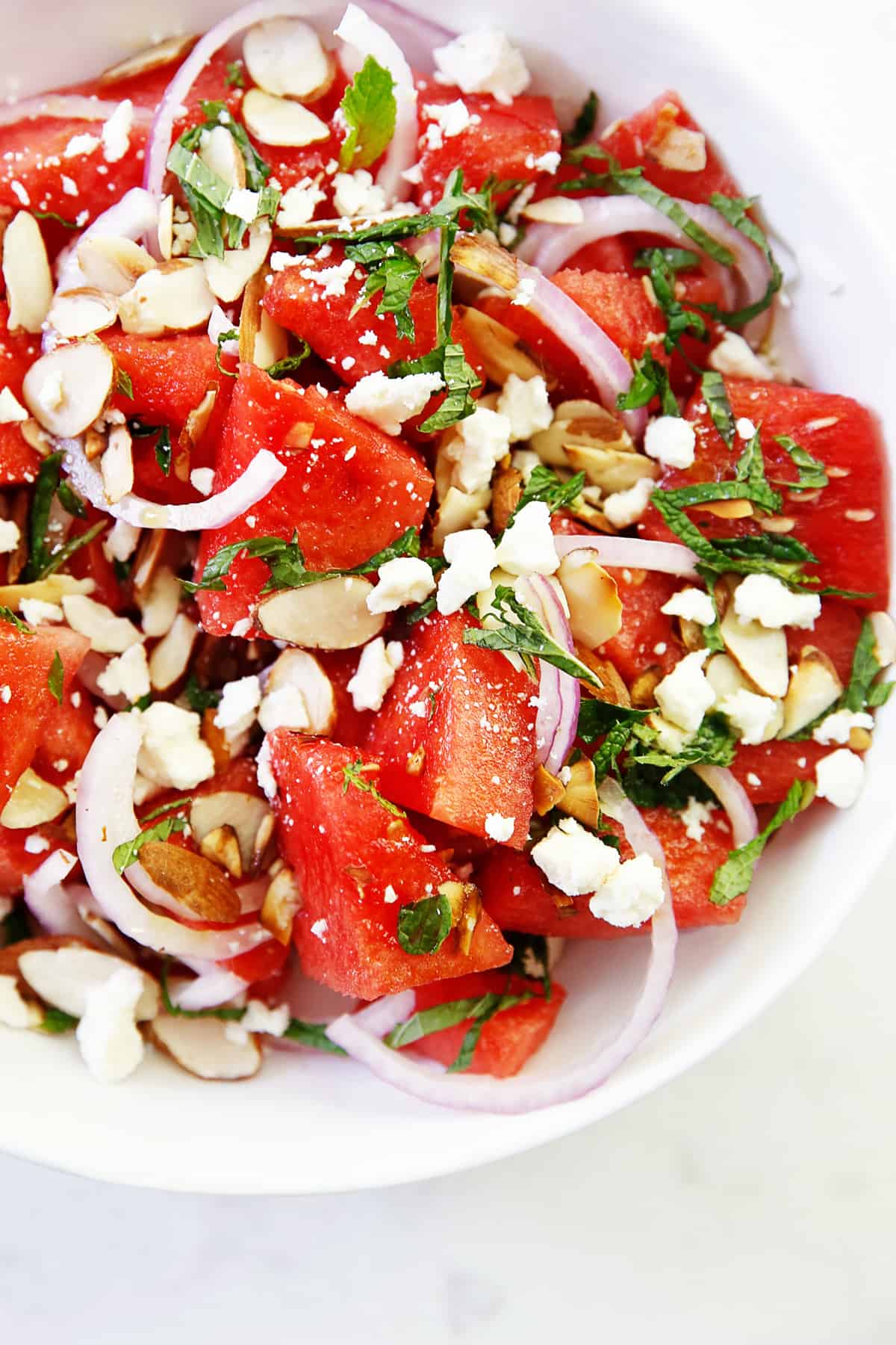 A bowl of watermelon salad with onions, herbs, cheese and nuts.
