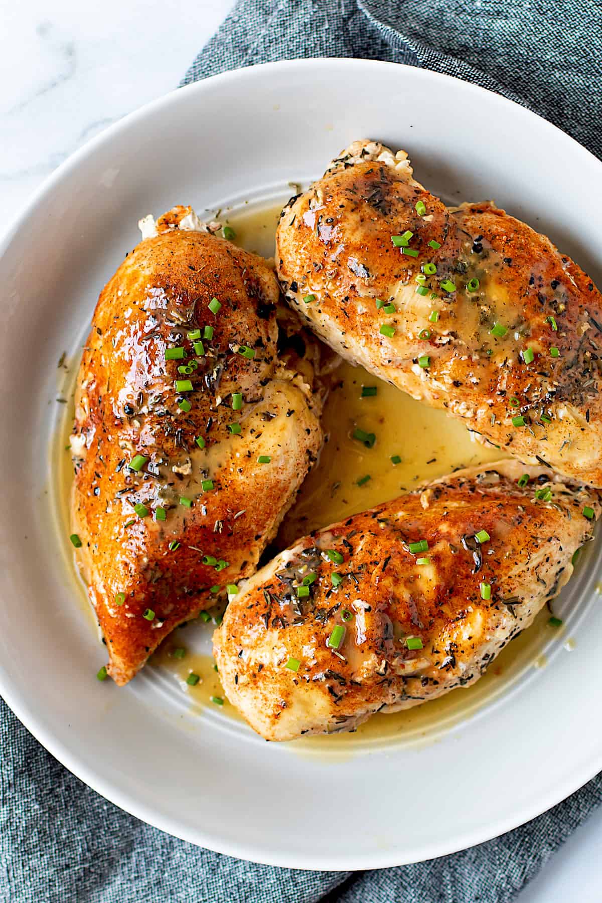 Fully cooked chicken breasts on a plate with pan sauce and herbs.