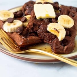 Chocolate waffles on a plate with butter and bananas.