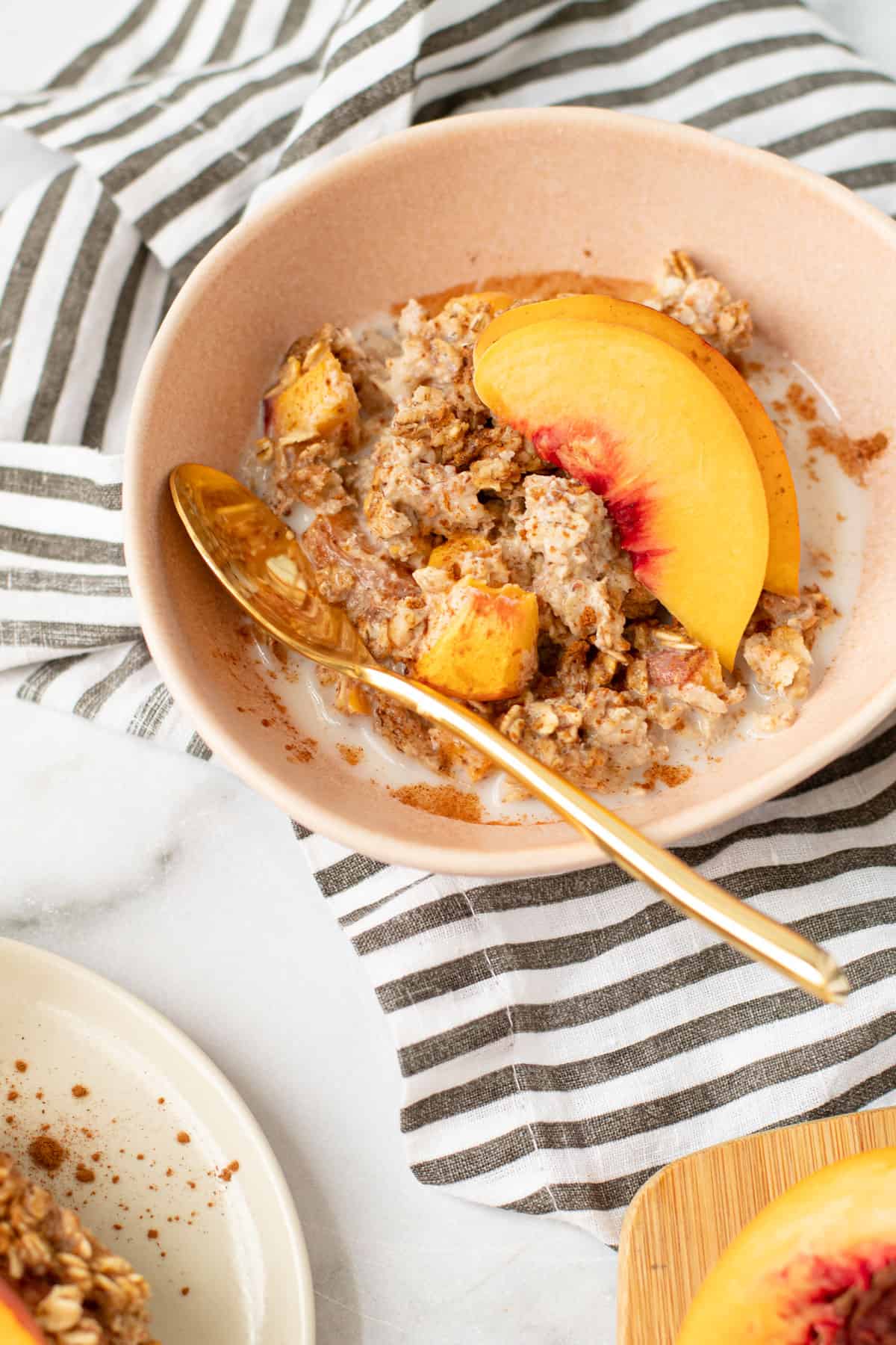 A bowl of vegan peaches and cream oatmeal with a spoon and some almond milk.