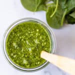 A jar of spinach basil pesto with a spoon in it.