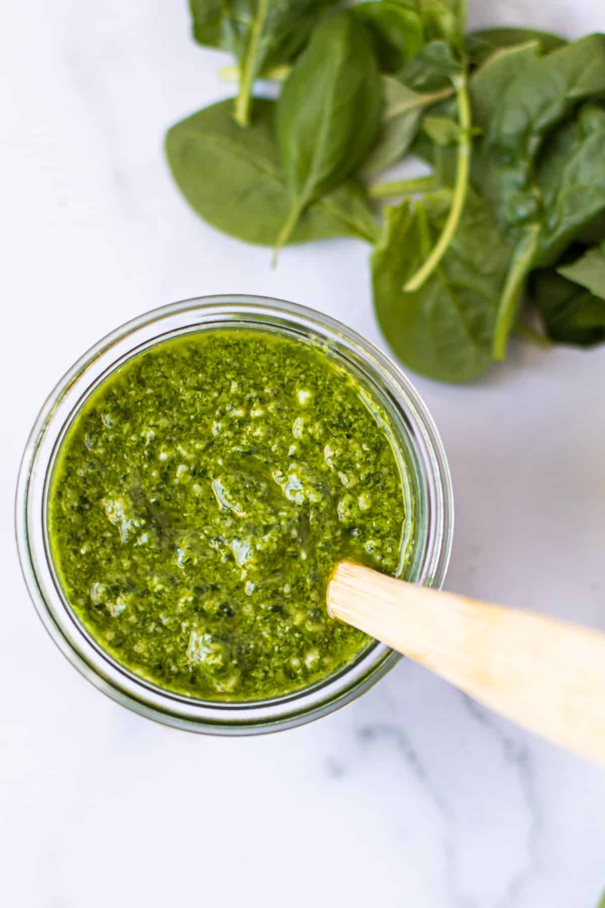 A jar of spinach basil pesto with a spoon in it.