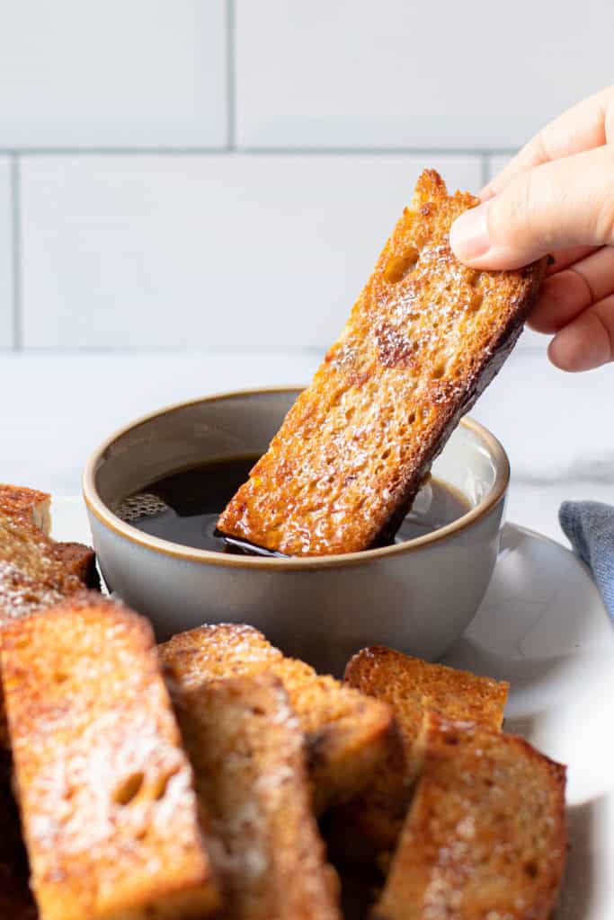 French toast sticks being dipped in maple syrup.