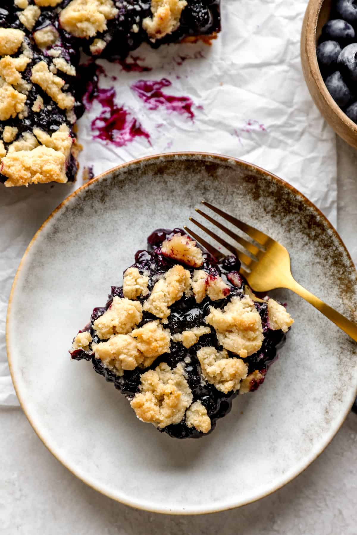 A blueberry crumb bar on a plate with a fork. 