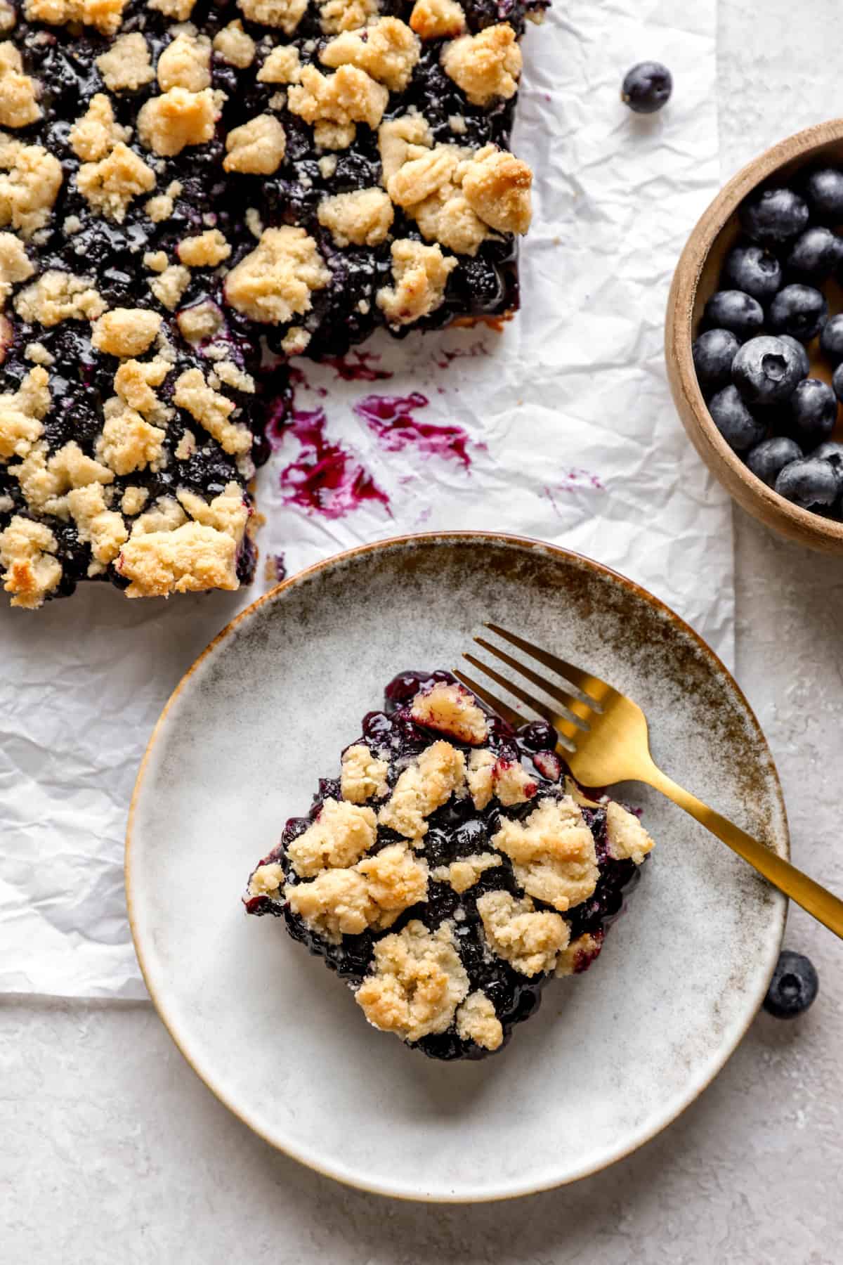 A blueberry crumb bar on a plate with a fork.