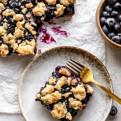 A blueberry crumb bar on a plate with a fork.
