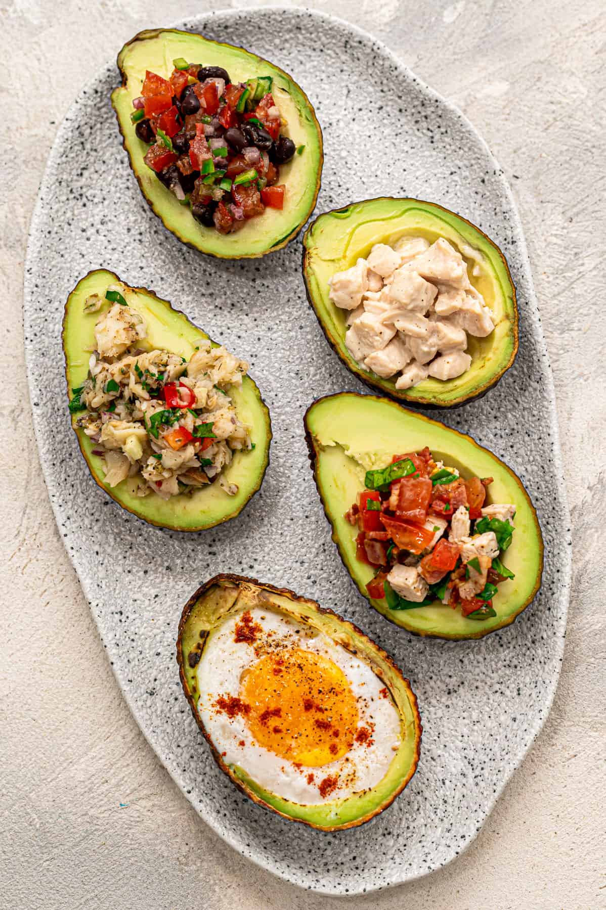 Five different avocado boats on a plate.