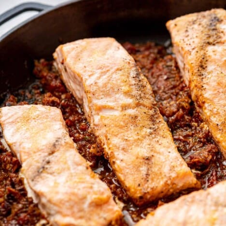 A skillet with salmon fillets in a puttanesca sauce.