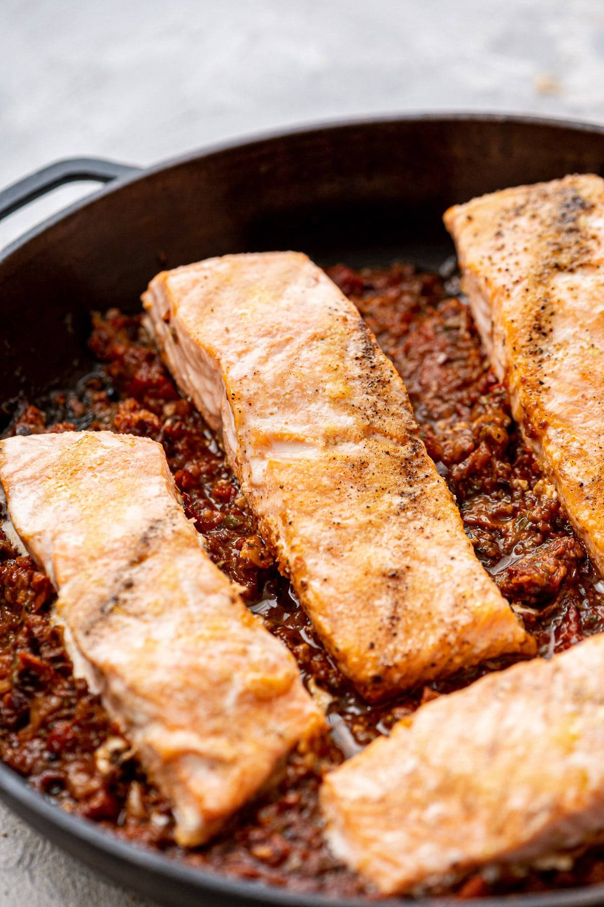 A skillet with salmon fillets in a puttanesca sauce.