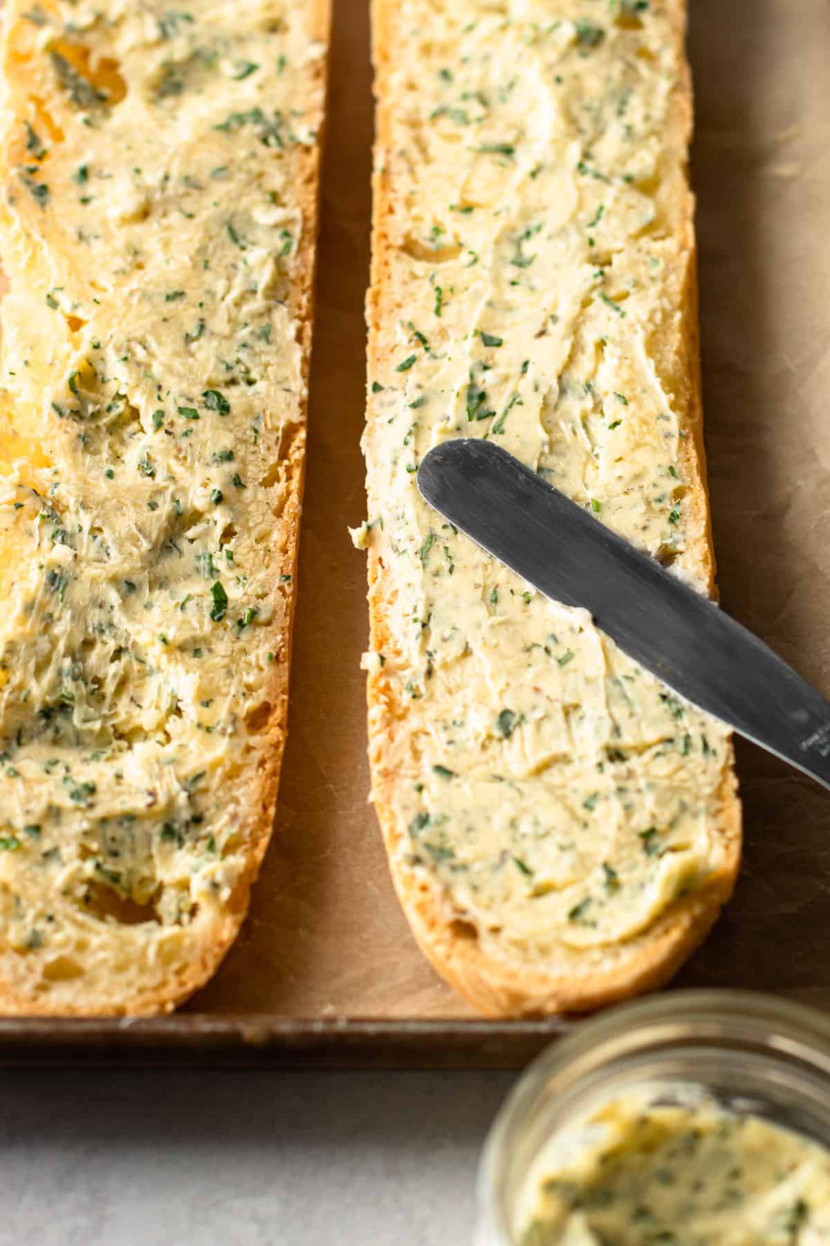 Spreading garlic butter on a gluten-free baguette.