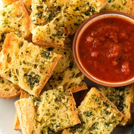 Sliced garlic bread piled up on a plate with marinara sauce for dipping.
