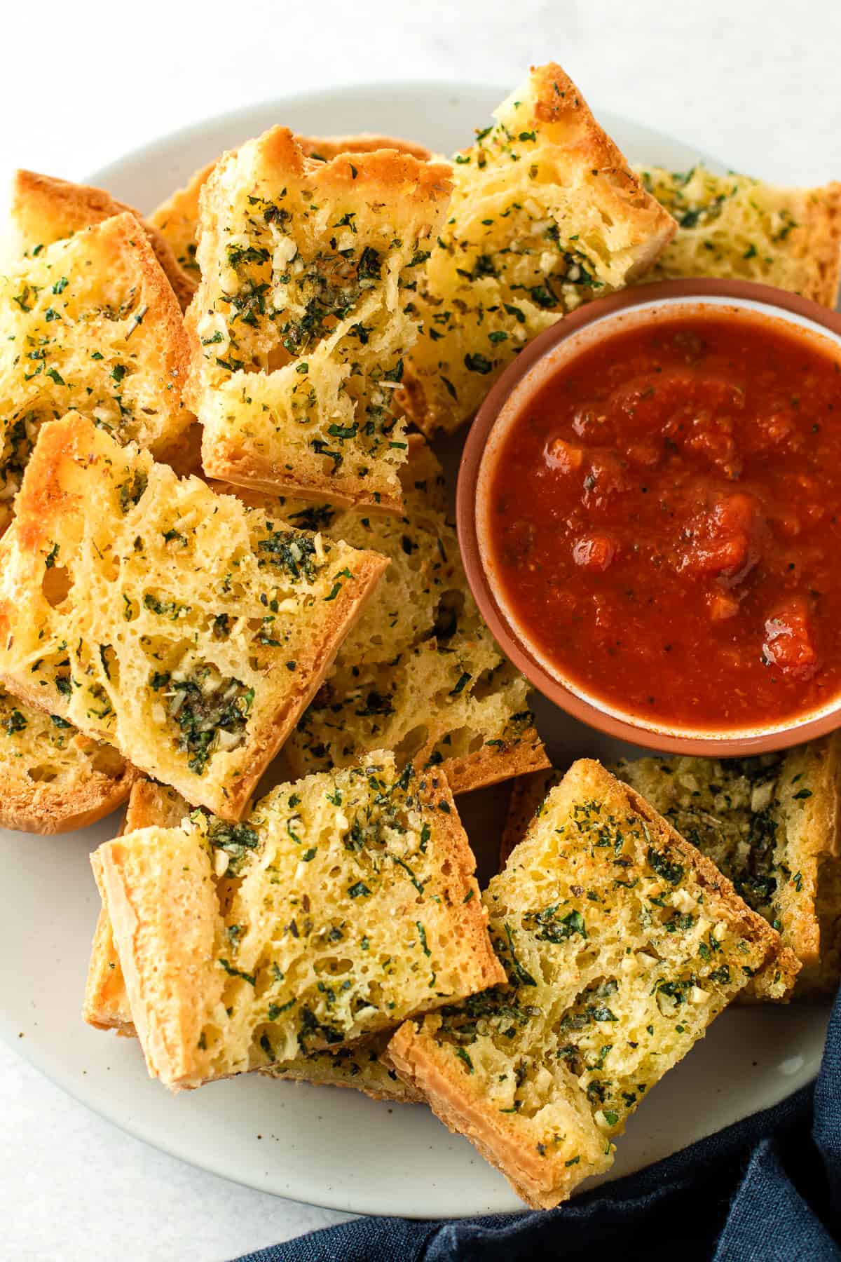 Sliced garlic bread piled up on a plate with marinara sauce for dipping.