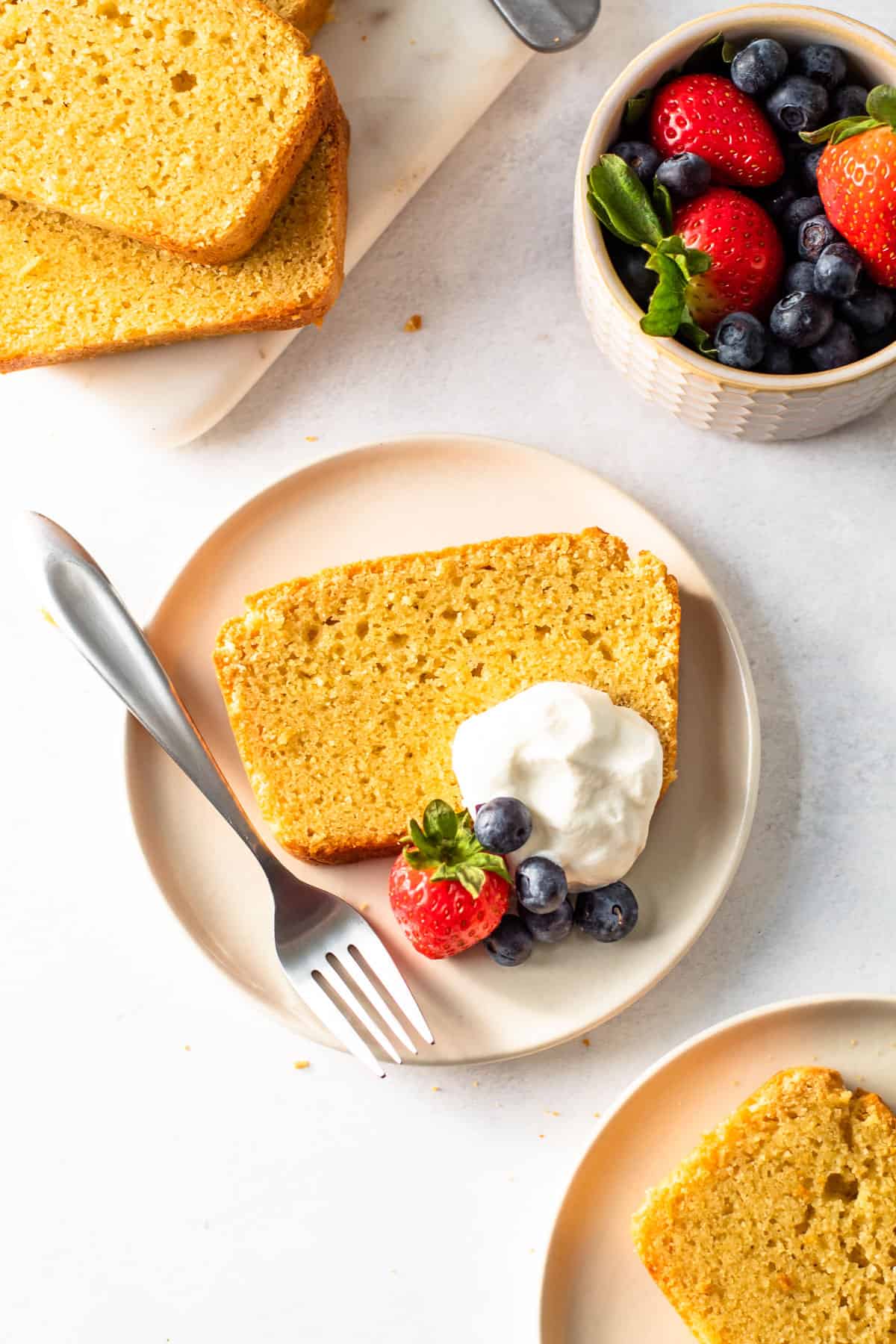 Gluten-free pound cake on a plate with whipped cream and berries.