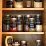 A cabinet full of spices decanted in a mason jar with a label.